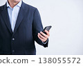 A faceless man in a suit stands facing forward against a white background, holding a smartphone. 138055572