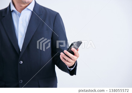 A faceless man in a suit stands facing forward against a white background, holding a smartphone. 138055572