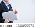 A faceless man in a suit stands at an angle against a white background, holding a laptop under his arm. 138055573