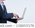 A man in a suit, his face obscured, is shown operating a laptop computer, photographed from the side against a white background. 138055576