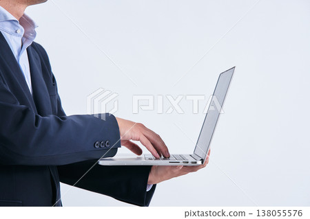 A man in a suit, his face obscured, is shown operating a laptop computer, photographed from the side against a white background. 138055576
