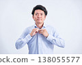 A Japanese man in his 30s changes his dress shirt in front of a white background, looking directly at the camera. 138055577