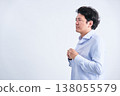A Japanese man in his 30s changing his dress shirt, photographed from an angle against a white background. 138055579
