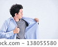 A man in his 30s changes his dress shirt in front of a white background, checking his appearance and checking for body odor. 138055580
