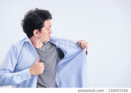 一位三十多歲的男子在白色背景前更換襯衫，檢查自己的儀容並檢查是否有體味。 138055580