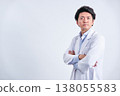 A confident and refreshing expression on the face of a male doctor in his 30s, wearing a white coat and with his arms crossed, against a white background. 138055583
