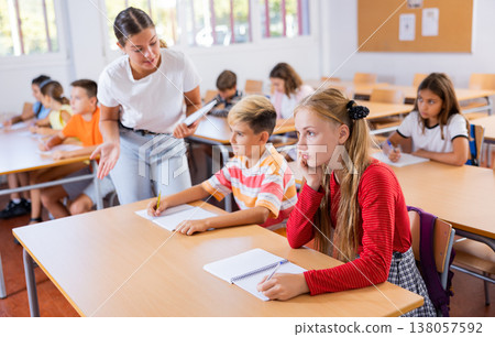 Friendly teacher woman helping children during lesson in schoolroom Friendly teacher woman helping children during lesson in schoolroom 138057592