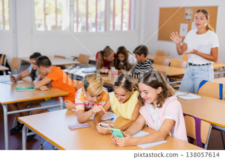 Interested preteen schoolchildren using phones during lesson in classroom Interested preteen schoolchildren using phones during lesson in classroom 138057614