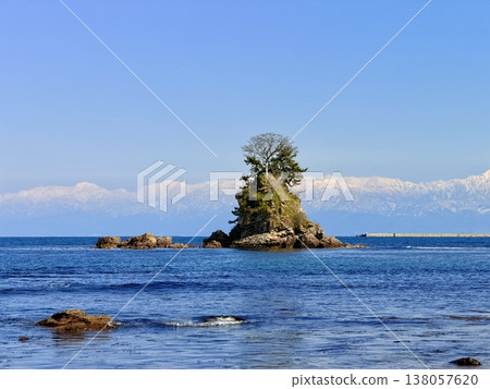 Onna-iwa Rock and the snow-covered Tateyama mountain range as seen from Amaharashi Coast in Takaoka City, Toyama Prefecture. 138057620