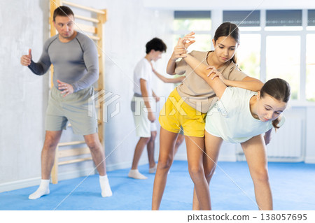 Two preteen girls train in pairs at self-defense lesson under guidance of trainer in gym 138057695