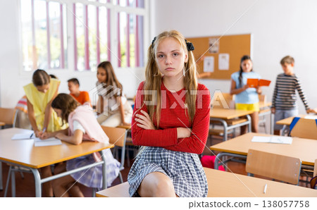 Sad bored girl sitting separately in classroom in break between lessons Sad bored girl sitting separately in classroom in break between lessons 138057758