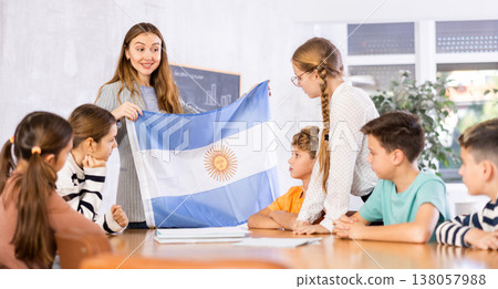 Female teacher, conducting extracurricular lesson in the school class tells schoolchildren the history of Argentina and shows national flag of country Female teacher, conducting extracurricular lesson in the school class tells schoolchildren the history of Argentina and shows national flag of country 138057988