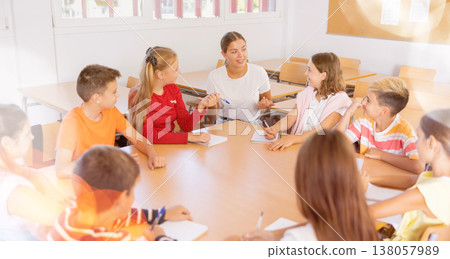 Female teacher conducting lesson with preteen children sitting around desk Female teacher conducting lesson with preteen children sitting around desk 138057989
