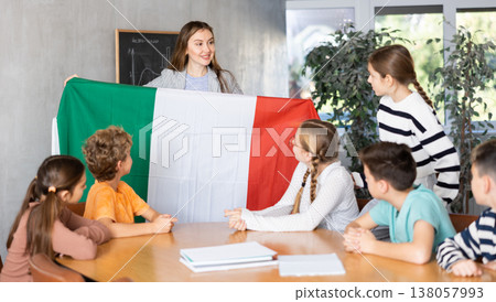 Joyful female teacher discussing with preteens students state flag of Italy in auditory of middle school Joyful female teacher discussing with preteens students state flag of Italy in auditory of middle school 138057993