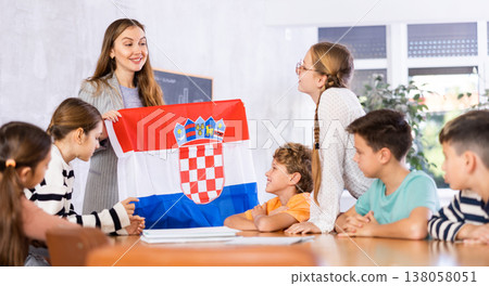 Smiling young woman teacher showing national flag of Croatia and telling preteens schoolchildren history of country during lesson in class Smiling young woman teacher showing national flag of Croatia and telling preteens schoolchildren history of country during lesson in class 138058051