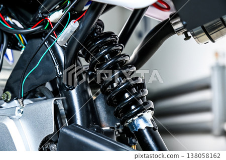 Close up of motorcycle rear shock absorber with black coil spring metal frame and electrical wiring parts in garage workshop with no people Close up of motorcycle rear shock absorber with black coil spring metal frame and electrical wiring parts in garage workshop with no people 138058162