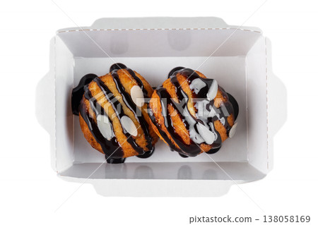 Sweet choux pastry with chocolate sauce and almond flake in white paper take out box on white background top view close up flat lay with copy space Sweet choux pastry with chocolate sauce and almond flake in white paper take out box on white background top view close up flat lay with copy space 138058169