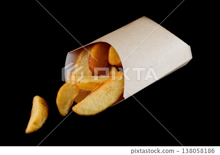 Crispy golden potato wedge in craft paper pocket on black background side view close up with copy space delicious savory american junk food snack Crispy golden potato wedge in craft paper pocket on black background side view close up with copy space delicious savory american junk food snack 138058186