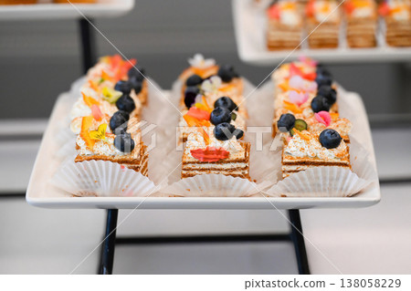 Catering dessert with honey cake medovik slices topped with cream and blueberry on buffet table for event decoration with no people close up Catering dessert with honey cake medovik slices topped with cream and blueberry on buffet table for event decoration with no people close up 138058229