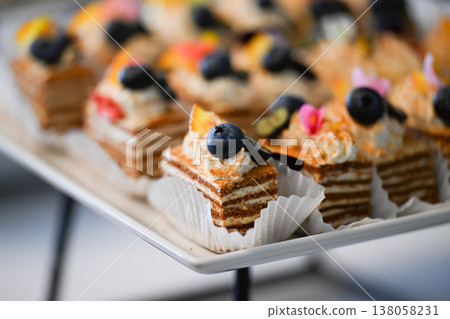 Catering dessert with honey cake medovik slices and blueberry in paper liner on buffet table for event decoration with no people and copy space Catering dessert with honey cake medovik slices and blueberry in paper liner on buffet table for event decoration with no people and copy space 138058231