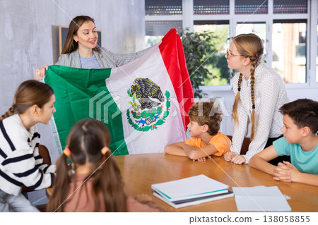 Female teacher, conducting extracurricular lesson in the school class tells schoolchildren the history of Mexico and shows national flag of country 138058855