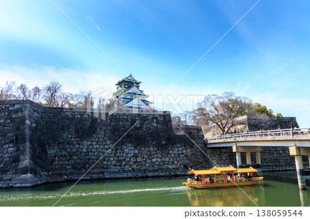 大阪城的主塔在藍天的襯托下格外醒目,一艘金色的遊船在護城河上巡遊。 大阪城的主塔在藍天的襯托下格外醒目,一艘金色的遊船在護城河上巡遊。 138059544