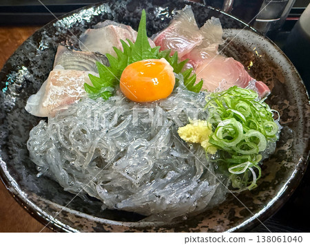 A seafood rice bowl topped with raw whitebait, sashimi, and an egg yolk. A seafood rice bowl topped with raw whitebait, sashimi, and an egg yolk. 138061040