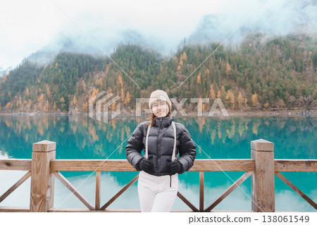 Happy woman traveler travel in jiuzhaigou national park in Sichuan, China. Tourist sightseeing Long lake and snow mountain in Autumn season. Famous Landmark and Vacation near Chengdu, China 138061549