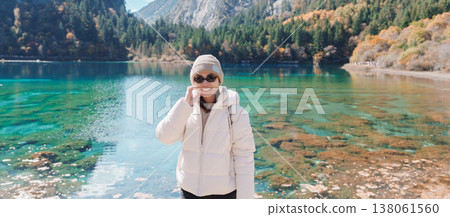 Happy woman traveler travel in jiuzhaigou national park in Sichuan, China. Tourist sightseeing Five Flower lake and snow mountain in Autumn season. Famous Landmark and Vacation near Chengdu, China Happy woman traveler travel in jiuzhaigou national park in Sichuan, China. Tourist sightseeing Five Flower lake and snow mountain in Autumn season. Famous Landmark and Vacation near Chengdu, China 138061560