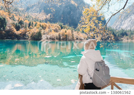 Happy woman traveler travel in jiuzhaigou national park in Sichuan, China. Tourist sightseeing Five Flower lake and snow mountain in Autumn season. Famous Landmark and Vacation near Chengdu, China 138061562