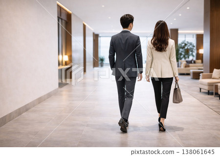 The backs of a male and female business person walking through a luxurious office lobby. 138061645
