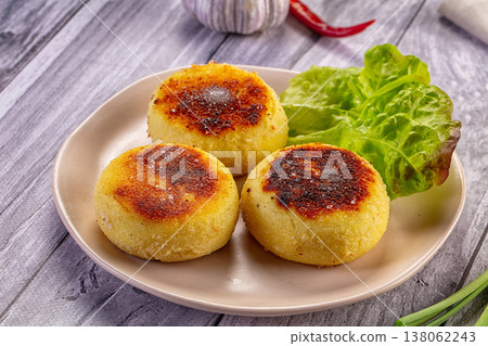 Homemade fried potato patties with fresh lettuce, garlic, and spring onion on a rustic wooden table. 138062243
