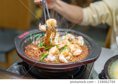 Woman tourist eating baked shrimp with glass noodles and garlic in restaurant. Popular foods for tourist eating in Chengdu, China. Chinese Asia and Sichuan foods concept Woman tourist eating baked shrimp with glass noodles and garlic in restaurant. Popular foods for tourist eating in Chengdu, China. Chinese Asia and Sichuan foods concept 138062784