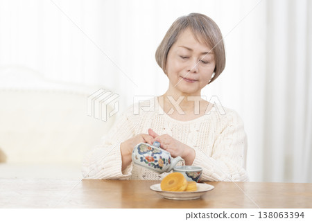 一位老婦人在客廳喝茶吃點心。 一位老婦人在客廳喝茶吃點心。 138063394