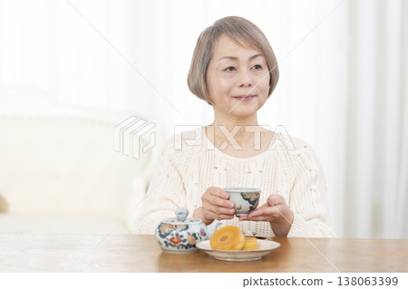 A senior woman drinking tea and snacks in the living room. 138063399