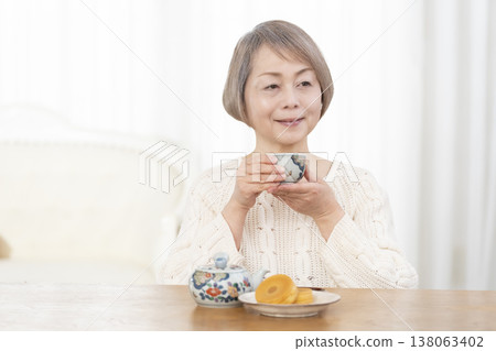 一位老婦人在客廳喝茶吃點心。 一位老婦人在客廳喝茶吃點心。 138063402