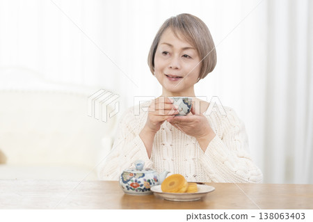 A senior woman drinking tea and snacks in the living room. A senior woman drinking tea and snacks in the living room. 138063403