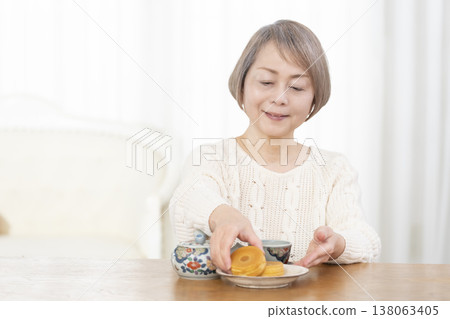A senior woman drinking tea and snacks in the living room. A senior woman drinking tea and snacks in the living room. 138063405