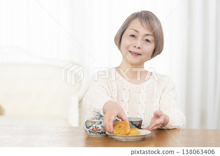 一位老婦人在客廳喝茶吃點心。 138063406