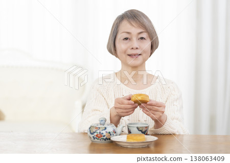 A senior woman drinking tea and snacks in the living room. 138063409