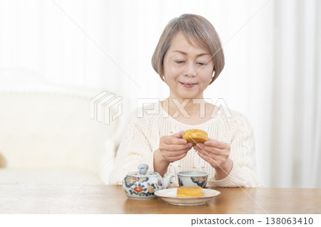 A senior woman drinking tea and snacks in the living room. A senior woman drinking tea and snacks in the living room. 138063410