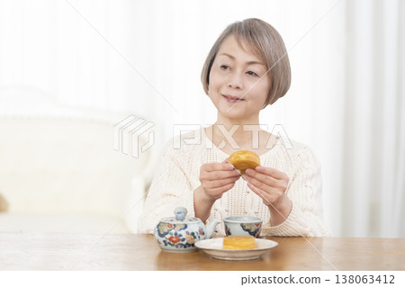 一位老婦人在客廳喝茶吃點心。 一位老婦人在客廳喝茶吃點心。 138063412