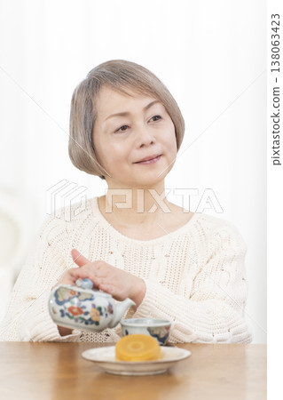 A senior woman drinking tea and snacks in the living room. 138063423