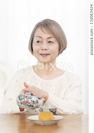 一位老婦人在客廳喝茶吃點心。 一位老婦人在客廳喝茶吃點心。 138063424
