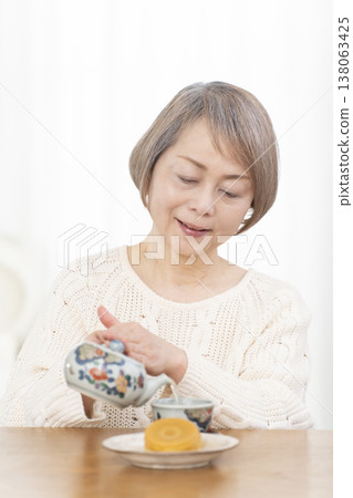 A senior woman drinking tea and snacks in the living room. 138063425