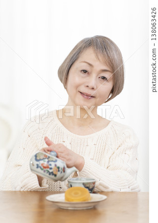 A senior woman drinking tea and snacks in the living room. 138063426