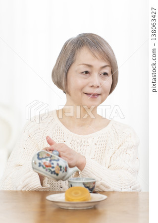 A senior woman drinking tea and snacks in the living room. 138063427