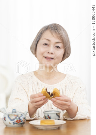 A senior woman drinking tea and snacks in the living room. A senior woman drinking tea and snacks in the living room. 138063442