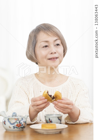 一位老婦人在客廳喝茶吃點心。 138063443