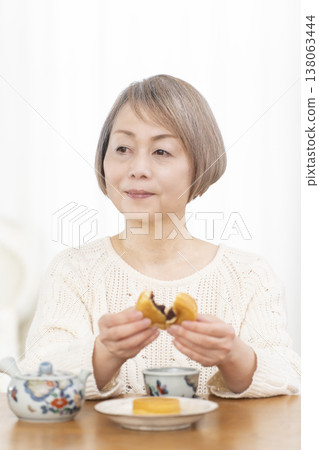 A senior woman drinking tea and snacks in the living room. 138063444